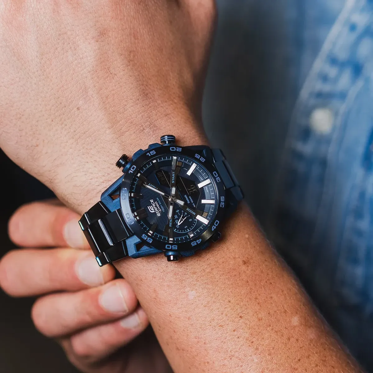 Reloj puesto en muñeca, toma cenital en primer plano, fondo desenfocado con prenda de mezclilla azul.