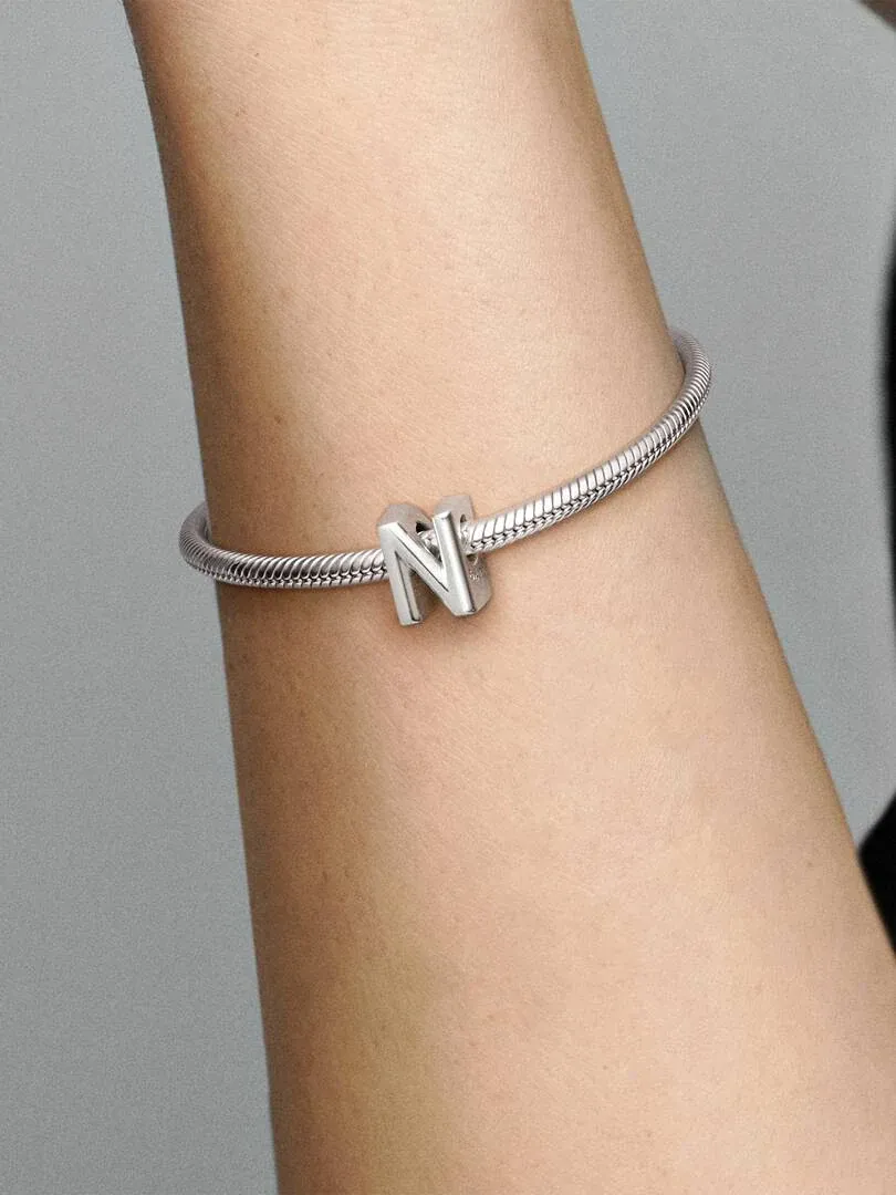 Primer plano de la letra N en plata sobre una pulsera, vista lateral en la muñeca con fondo neutro.