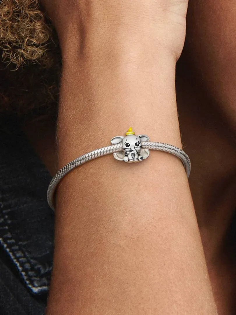 Close-up of the Dumbo charm on a silver bracelet, worn on a wrist with a blurred background.