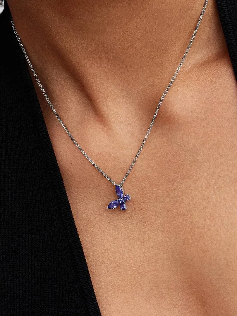 Nahaufnahme des blauen Schmetterlingsanhängers am Hals eines Models, Frontansicht vor dunklem Hintergrund.