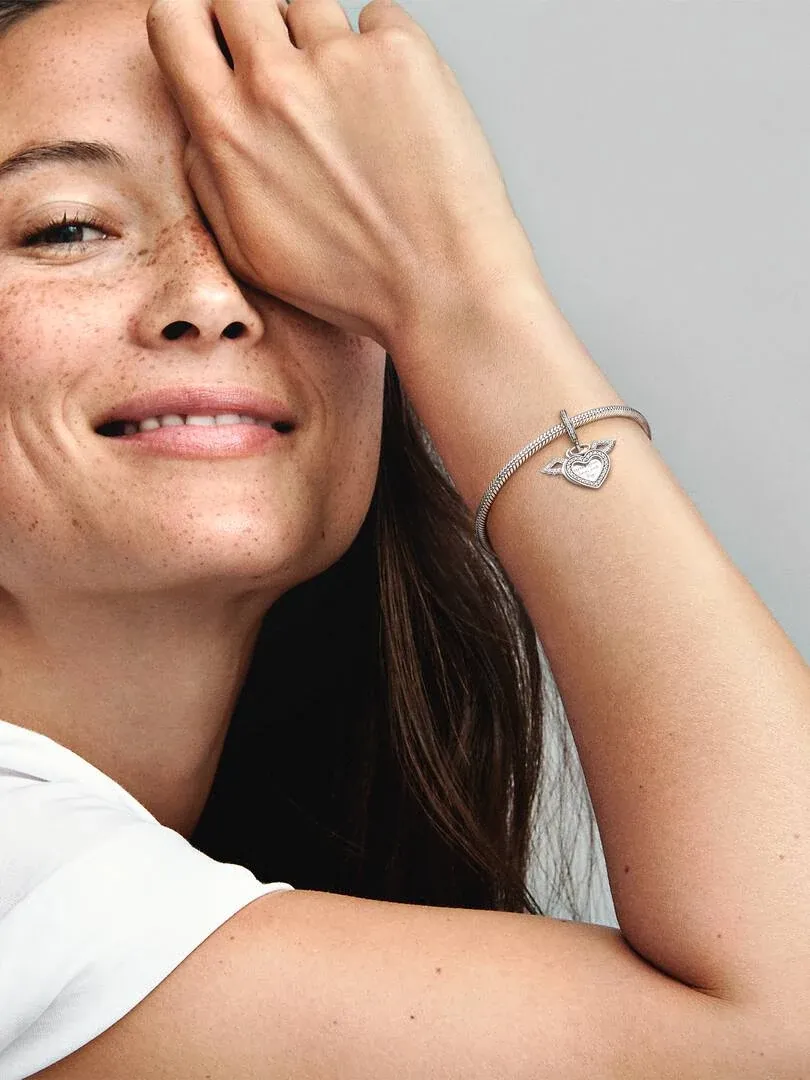 Close-up van een vrouw met de engelenvleugels charm om haar pols, zijaanzicht tegen een neutrale grijze achtergrond.