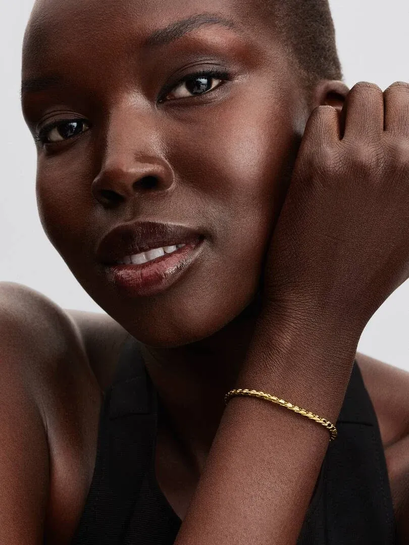 Nahaufnahme des goldenen Armbands am Handgelenk, Seitenansicht mit Modell vor hellem neutralem Hintergrund.