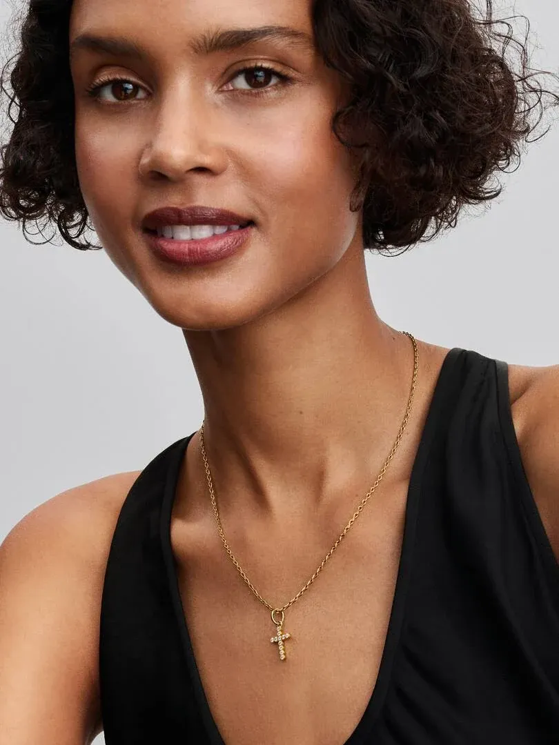 Close-up van kruis hanger ketting om de hals, model met zwarte top tegen neutrale achtergrond.