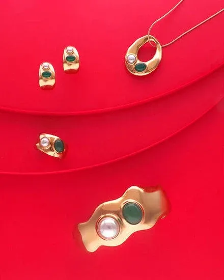 Earrings and necklace set on wavy red background, top-down view of gold jewelry pieces.