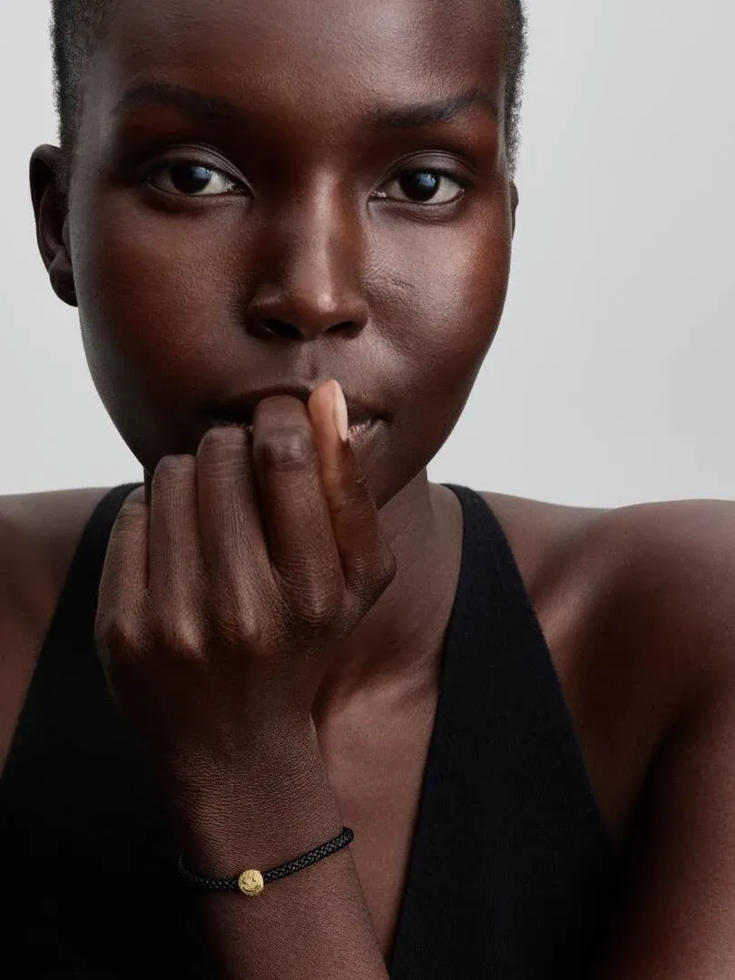 Close-up van een model met de gouden charm om de pols, vooraanzicht met neutrale achtergrond.