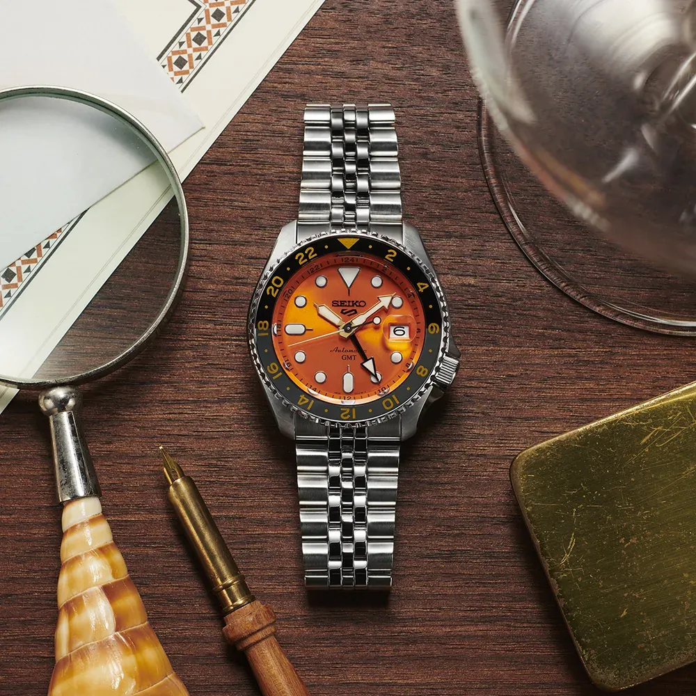 Top view of the watch on dark wood background, styled with a magnifying glass, pen, and gold accessory