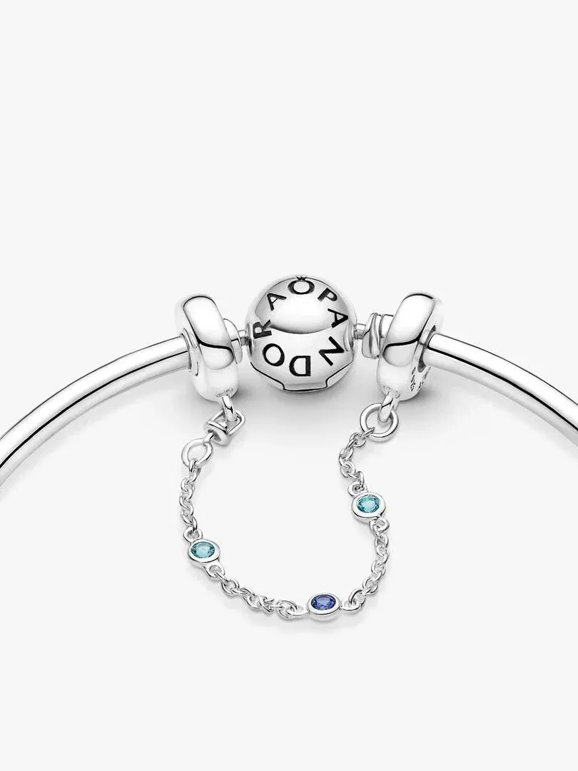 Primer plano de la cadena de seguridad con tres cristales azules sujeta a una pulsera, fondo blanco.