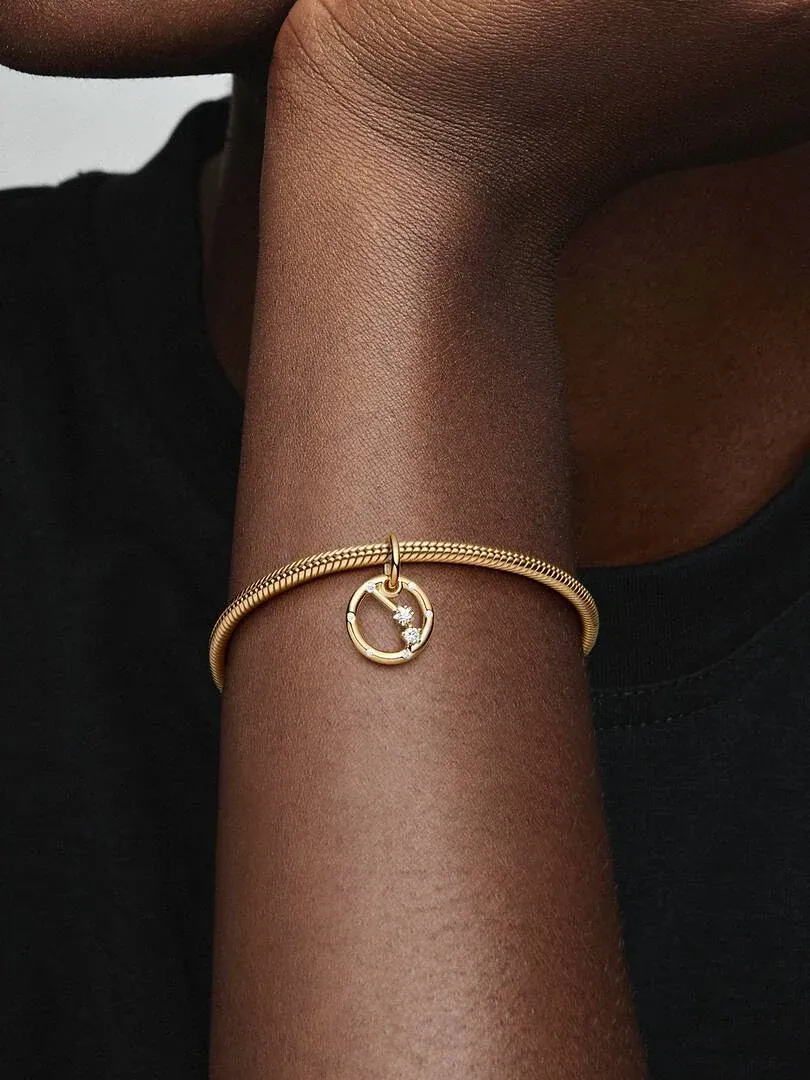 Close-up van een pols met de Aries charm aan een gouden armband, tegen een zwarte achtergrond.