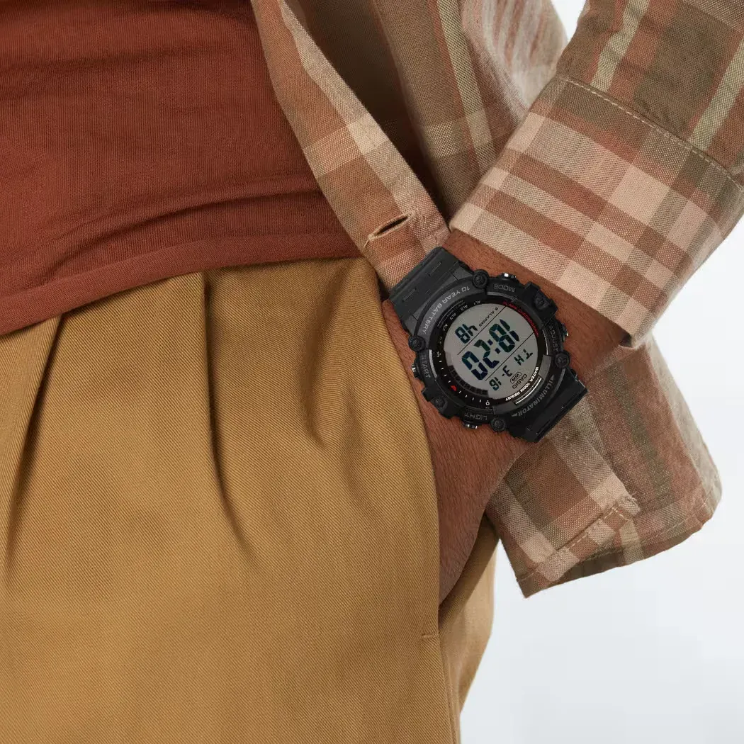 Reloj digital negro puesto en la muñeca de un modelo con camisa de cuadros y pantalones caqui, plano detalle.
