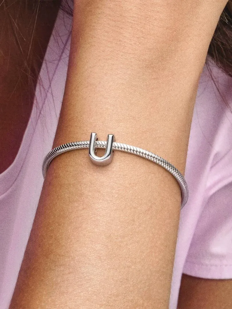 Close-up of a silver letter U charm on a bracelet, worn on a wrist.