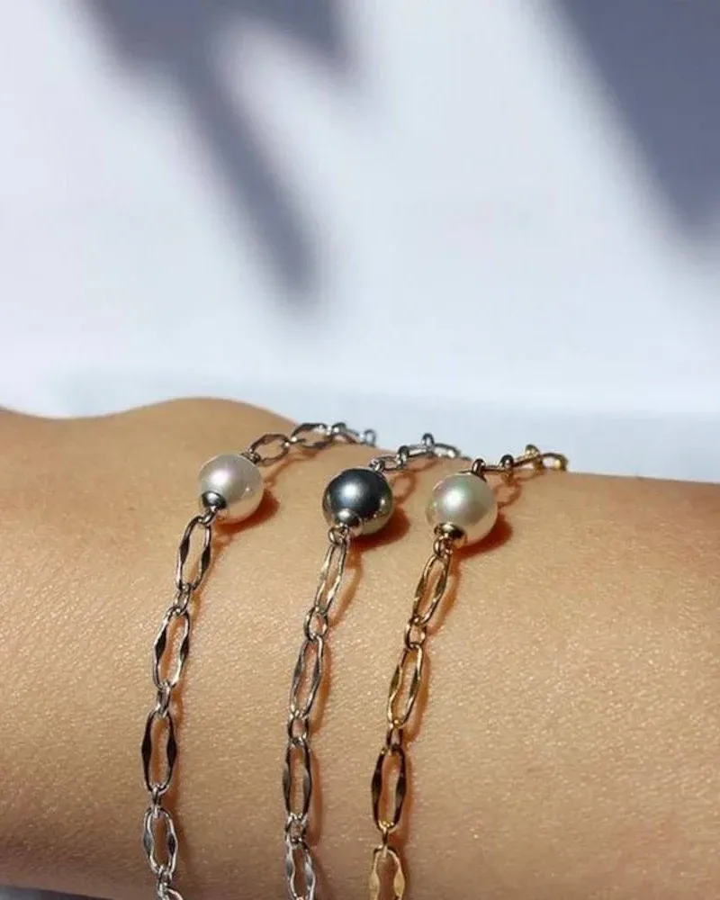 Close-up van drie armbandjes met parels om een pols, zijaanzicht met wazige achtergrond.