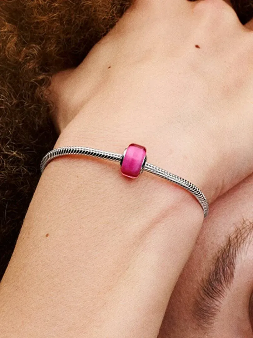 Gros plan d'un charm rose sur un bracelet en argent porté au poignet, vue de côté avec fond flou.