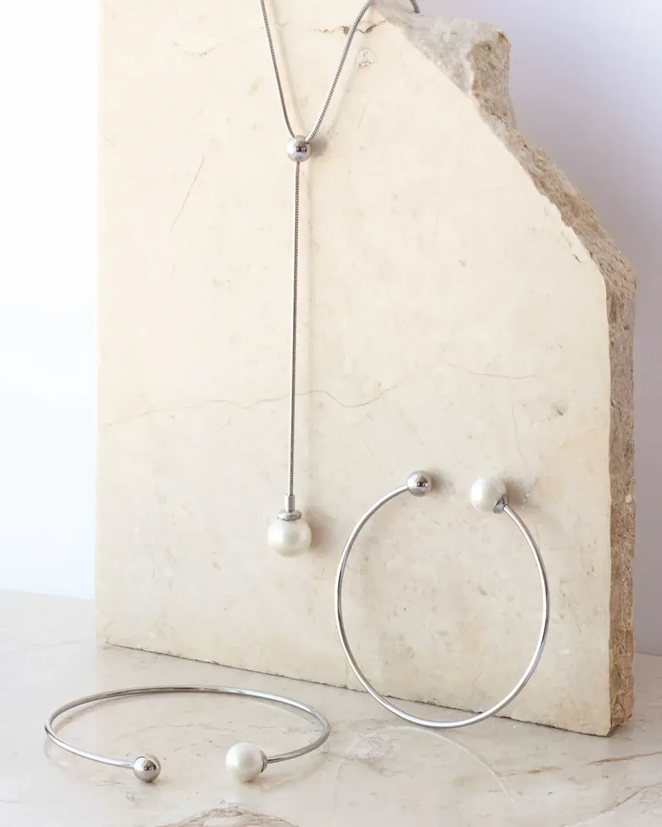 Composición de joyería con collar y brazaletes sobre bloque de piedra natural, fondo blanco.