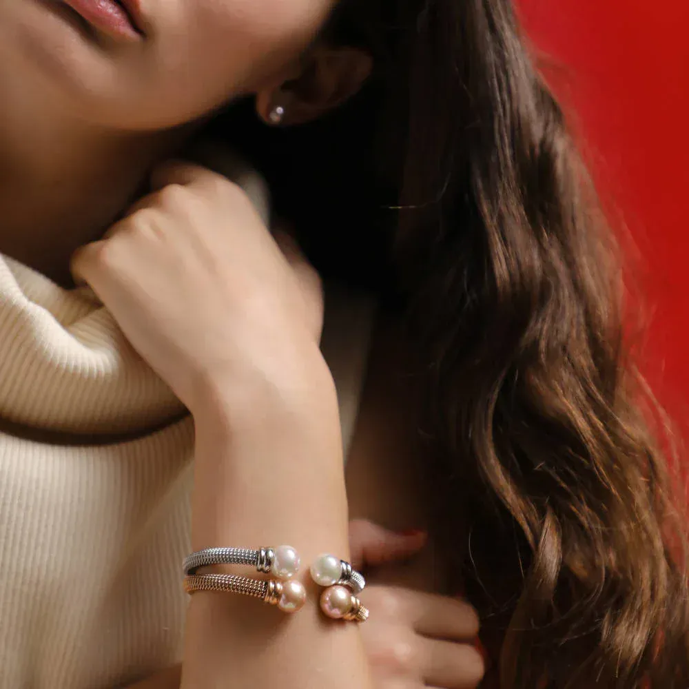 Brazaletes de malla y perlas puestos en muñeca, modelo con jersey blanco sobre fondo rojo