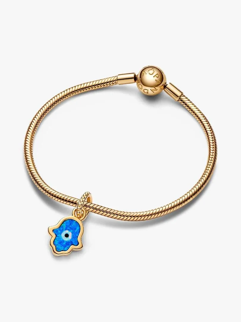 Charm Hamsa azul sobre pulsera de cordón dorado, vista frontal en ángulo, fondo blanco.