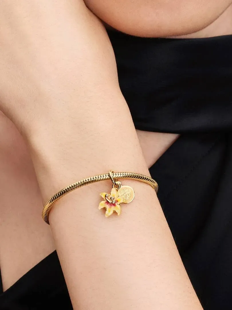 Nahaufnahme des Blumen-Charms an einem goldenen Armband, getragen am Handgelenk vor unscharfem dunklem Hintergrund.
