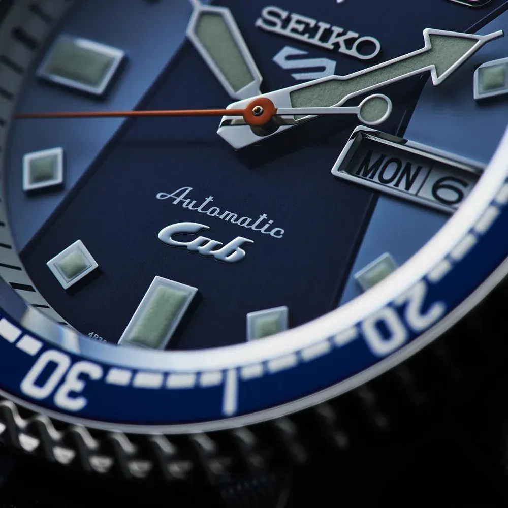 Macro close-up of the blue dial, 'Cub' logo detail, orange seconds hand and date window