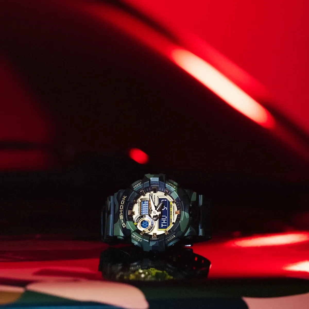 Reloj centrado sobre superficie reflectante con fondo rojo dramático y luces difuminadas.