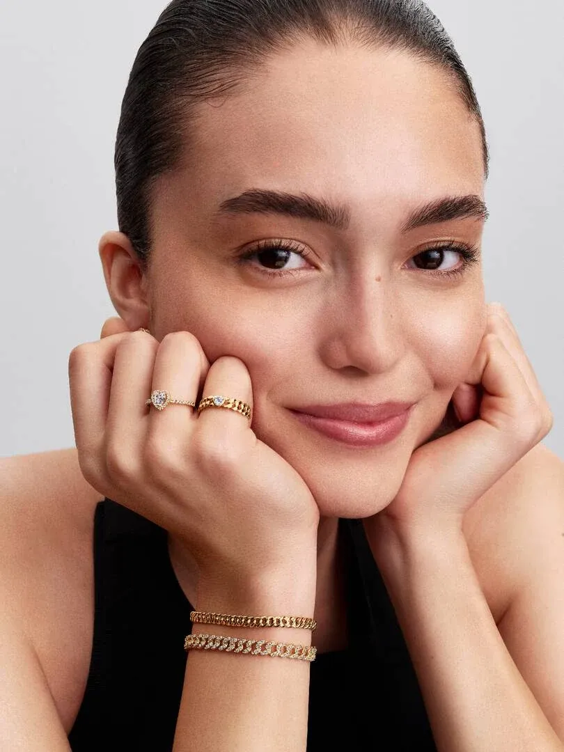 Gros plan d'un modèle portant une bague chaîne avec cœur en zircon, mains près du visage, fond neutre.