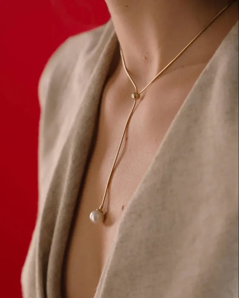Gros plan du collier avec perle sur le cou et le décolleté, fond rouge vif.