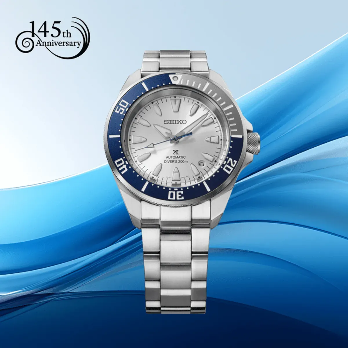 Reloj visto de frente sobre fondo sintético de ondas azules con logotipo de 145 aniversario en la esquina superior.