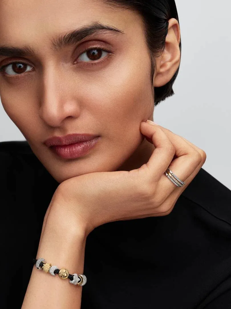 Close-up van een vrouw met een charm-armband om haar pols, zijaanzicht rustend tegen haar gezicht.