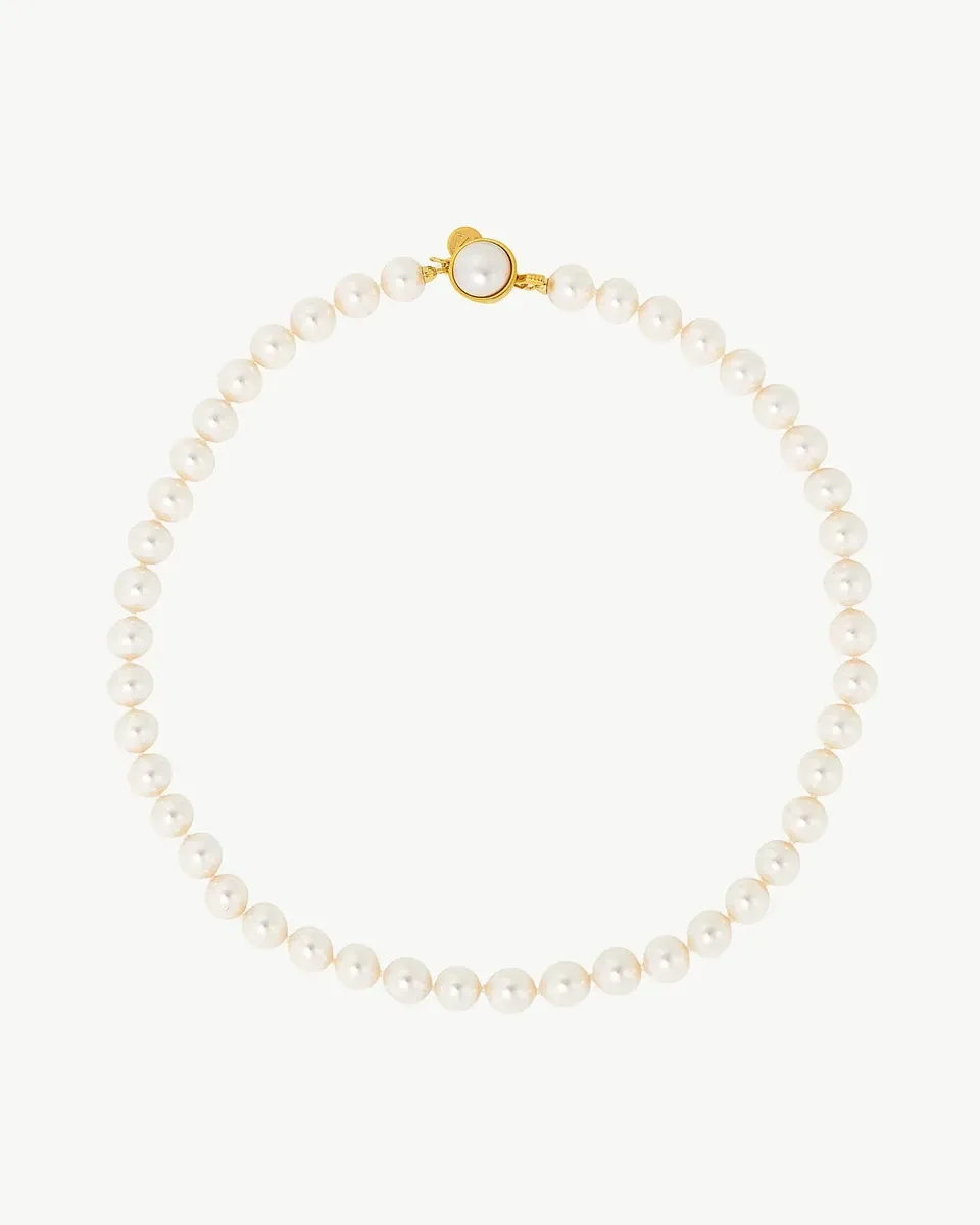 Collar de perlas dispuesto en círculo sobre fondo blanco, vista cenital con detalle del cierre dorado.