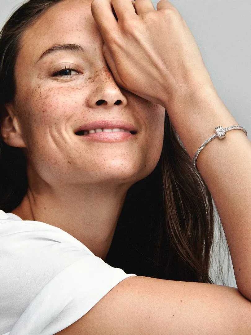 Nahaufnahme des Clip-Charms am Handgelenk, lächelndes Modell vor hellem neutralem Hintergrund.