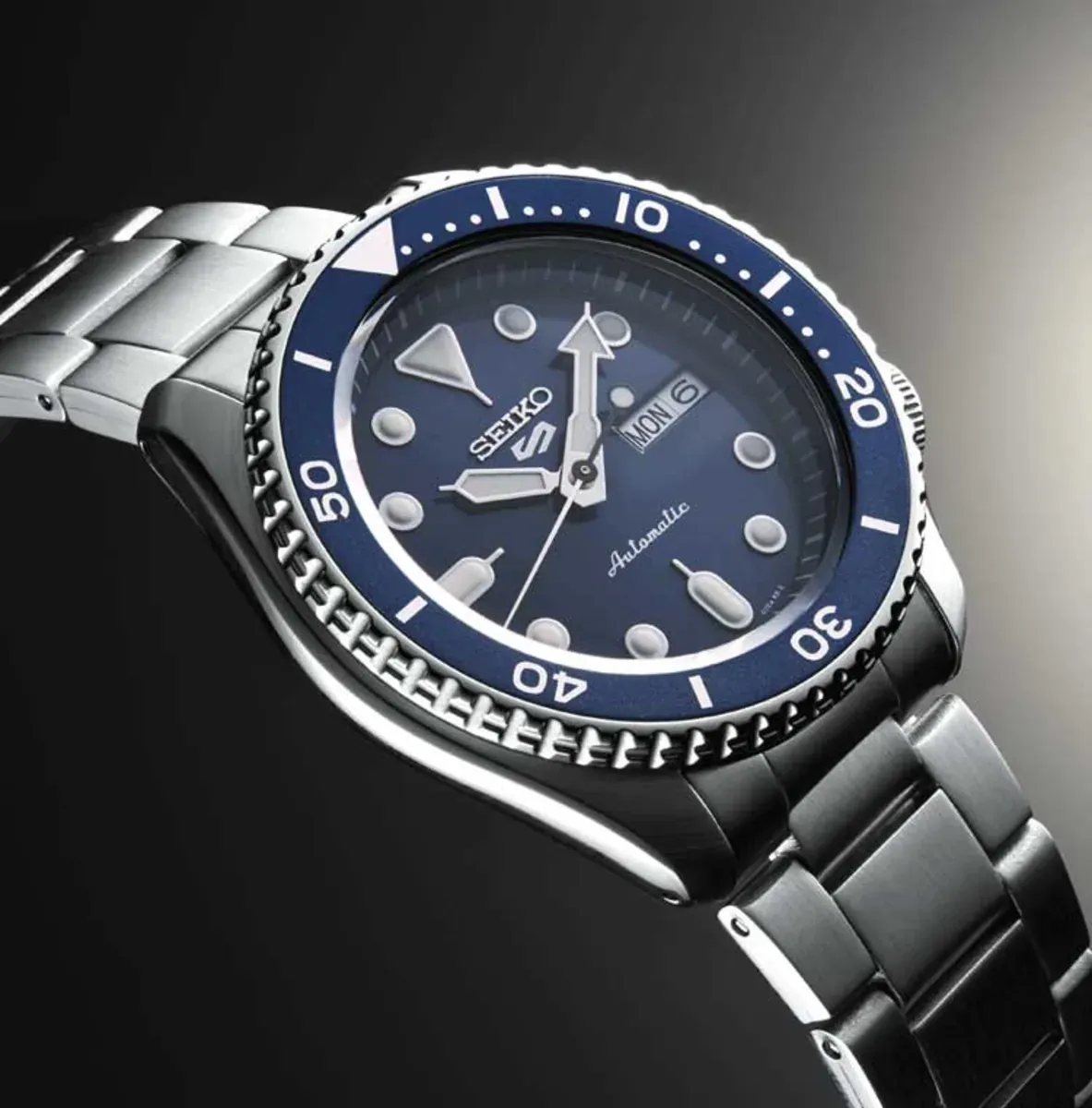 Prise de vue en perspective de la montre, focus sur le cadran bleu et la lunette, sur fond dégradé sombre.