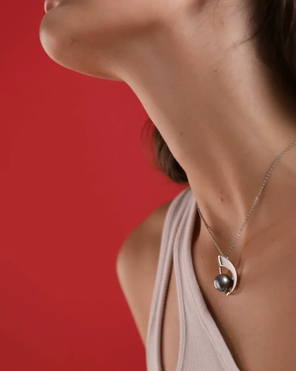 Close-up van de grijze parelketting om de hals van een model tegen een levendige rode achtergrond.
