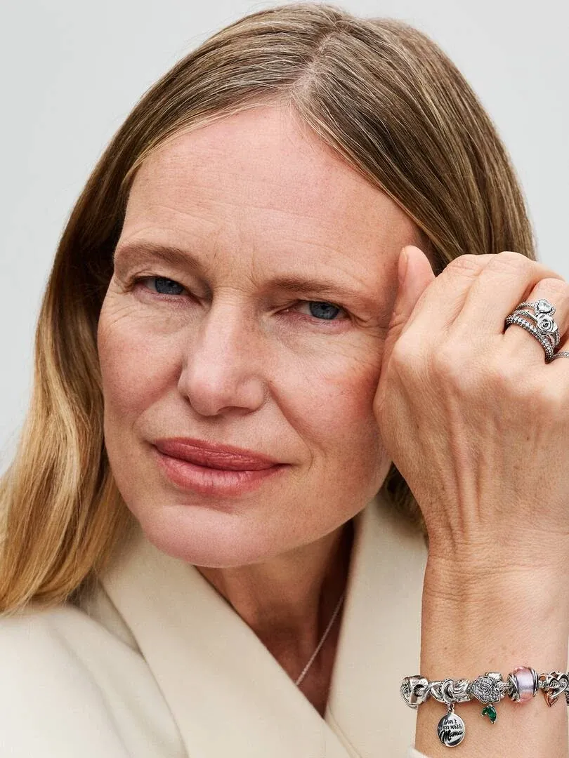 Close-up of hand wearing charm bracelet and ring, model posing with hand near face.
