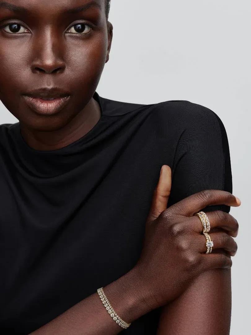 Close-up van hand en pols met tennisarmband en ring, model in zwart shirt, lichtgrijze achtergrond.