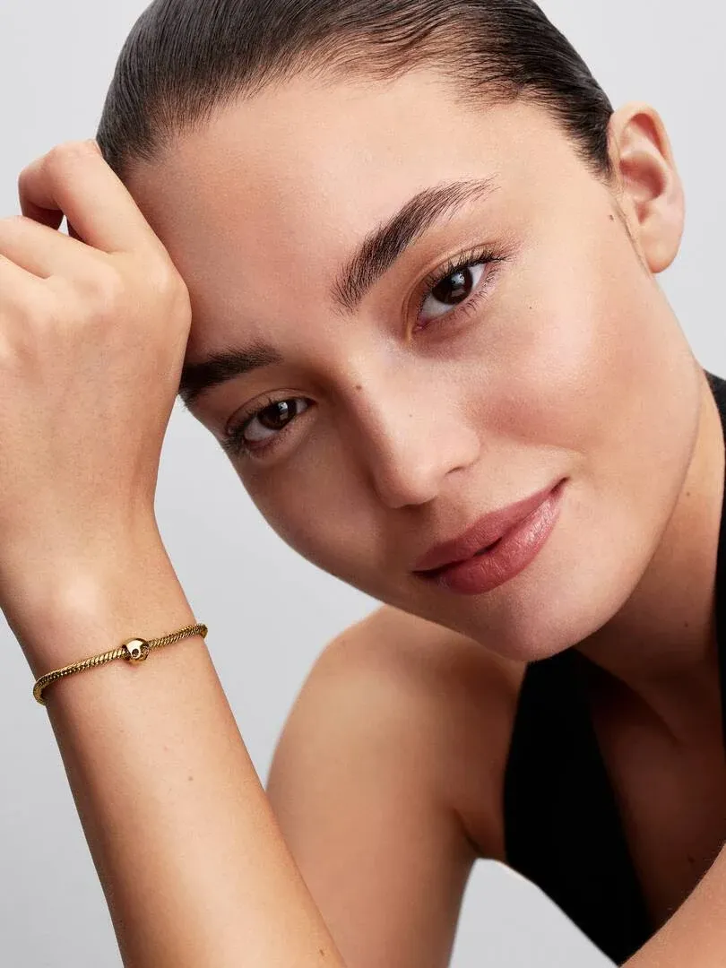 Nahaufnahme eines Models mit dem Charm am Handgelenk, Seitenansicht vor hellem neutralem Hintergrund.