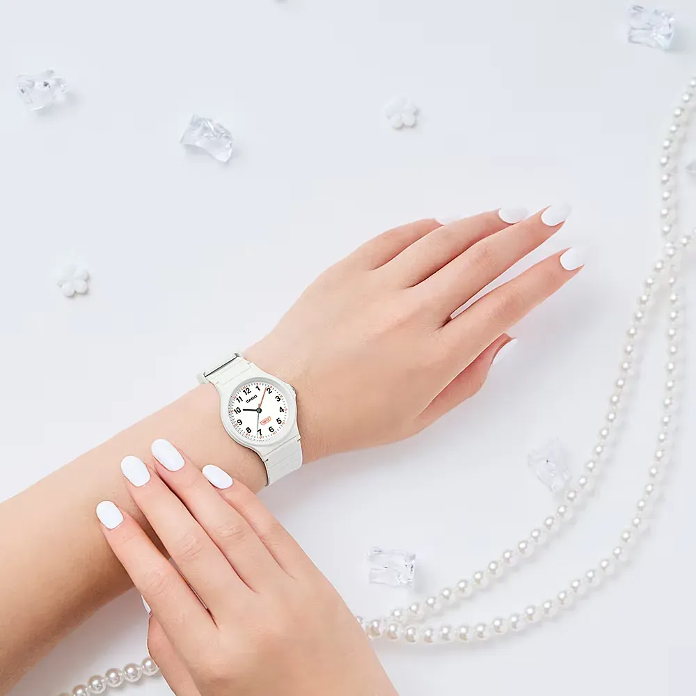 Primer plano del reloj blanco puesto en la muñeca, uñas blancas, fondo blanco con perlas y cristales decorativos.