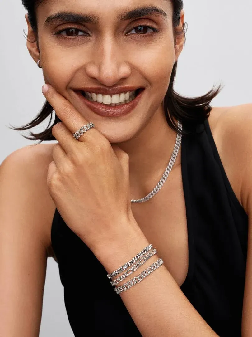 Lächelndes Modell mit Cuban Link Halskette und Armbändern, Medium Shot vor neutralem Hintergrund.