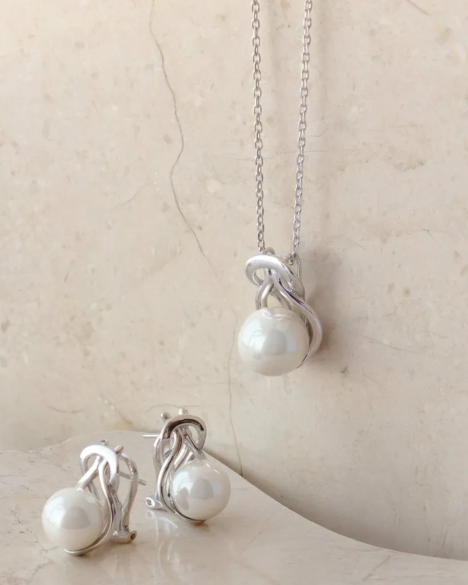 Conjunto de collar y pendientes con perlas sobre superficie de mármol beige, toma frontal con luz suave.