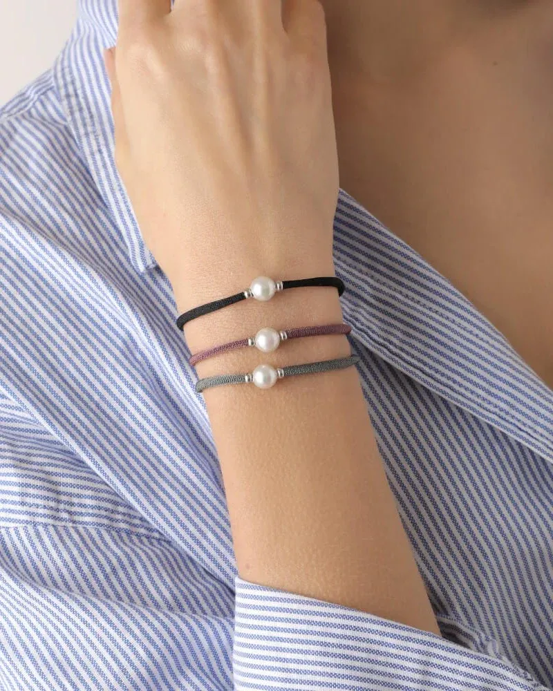 Primer plano de tres pulseras de perlas sobre la muñeca, toma lateral con camisa a rayas azul y blanca.