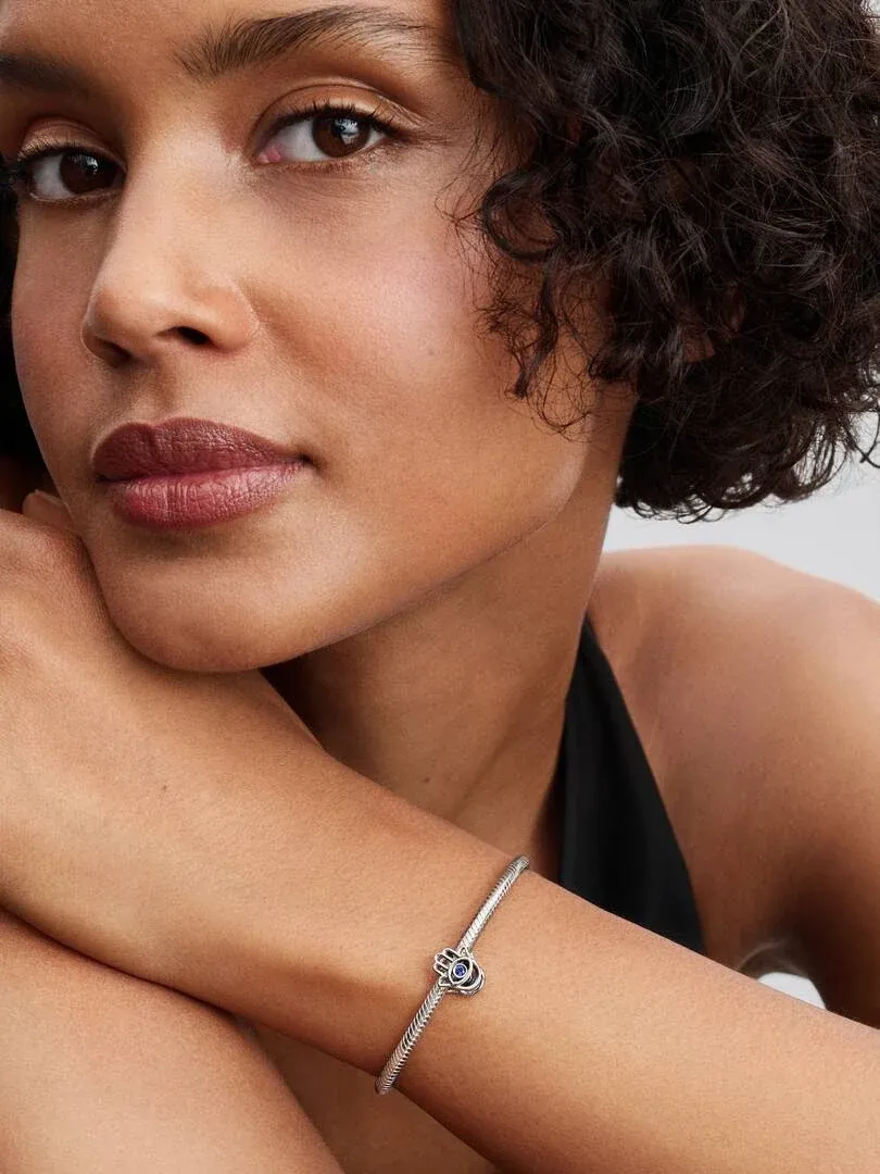 Gros plan d'un bracelet avec charm Main de Fatima sur le poignet d'un modèle, fond neutre flou.