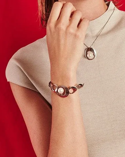 Collar y pulsera con perla blanca sobre modelo, toma de medio cuerpo con fondo rojo vibrante.