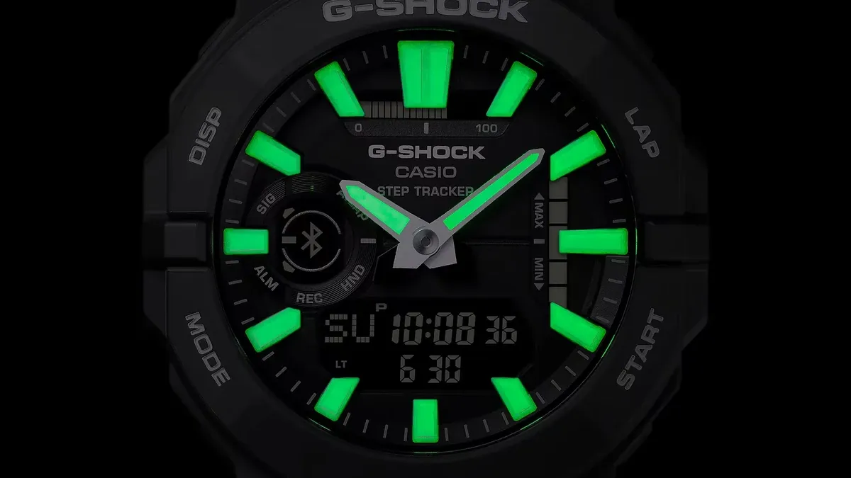 Primer plano frontal de la esfera del reloj con índices y agujas luminiscentes verdes sobre fondo negro.