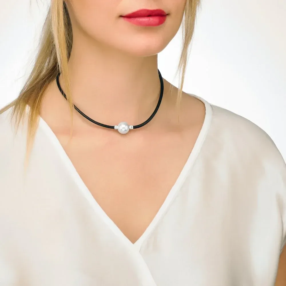 Close-up of the black leather necklace with a white pearl on a model's neck, light neutral background.
