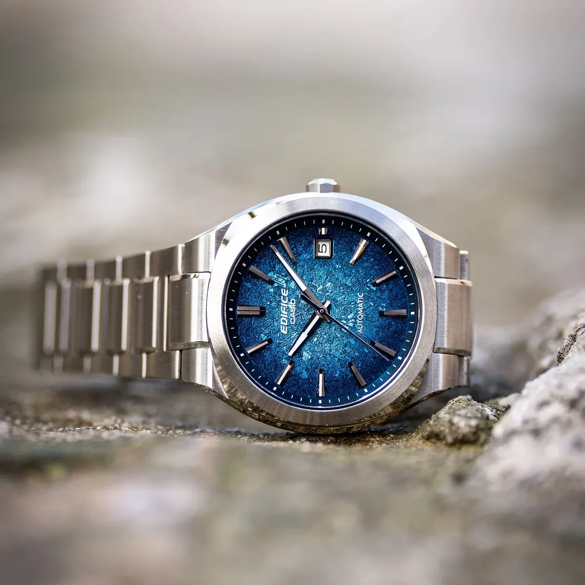 Reloj apoyado sobre una superficie de piedra rugosa, toma en primer plano con fondo desenfocado.