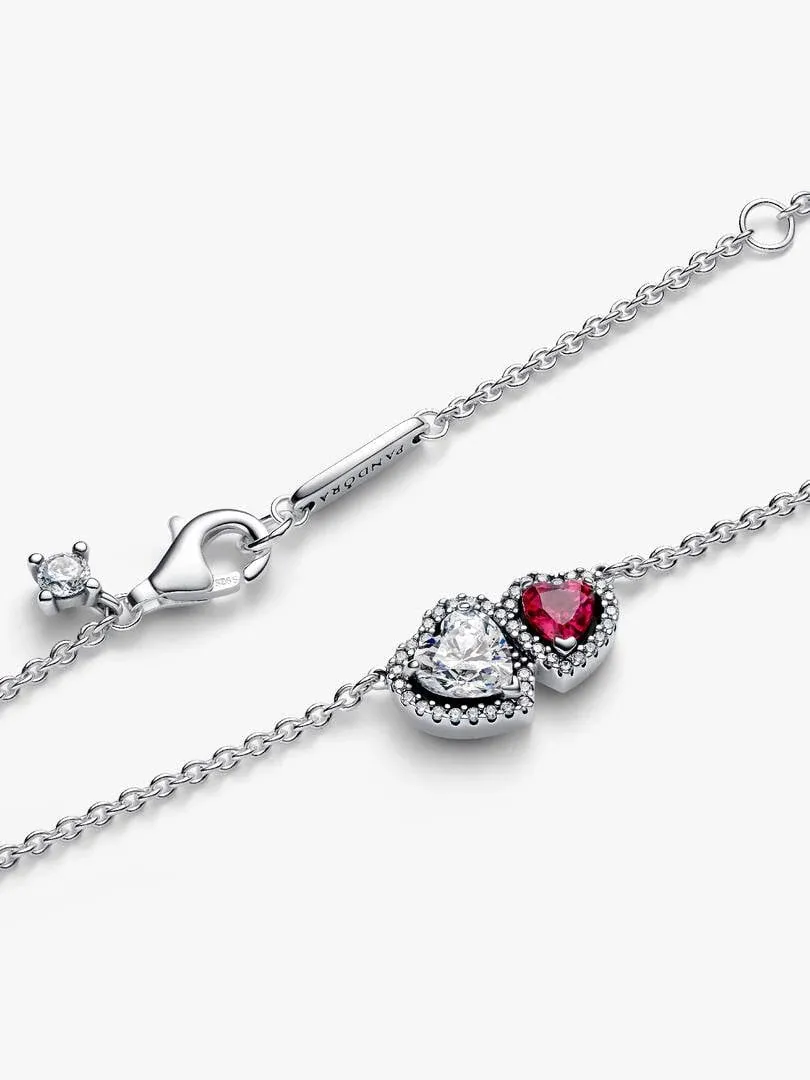 Diagonal close-up of heart pendants with red and clear stones on a silver chain.