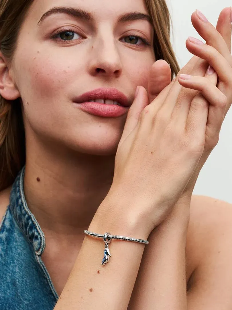 Close-up of a model wearing the blue slipper charm on a silver bracelet, side view shot.