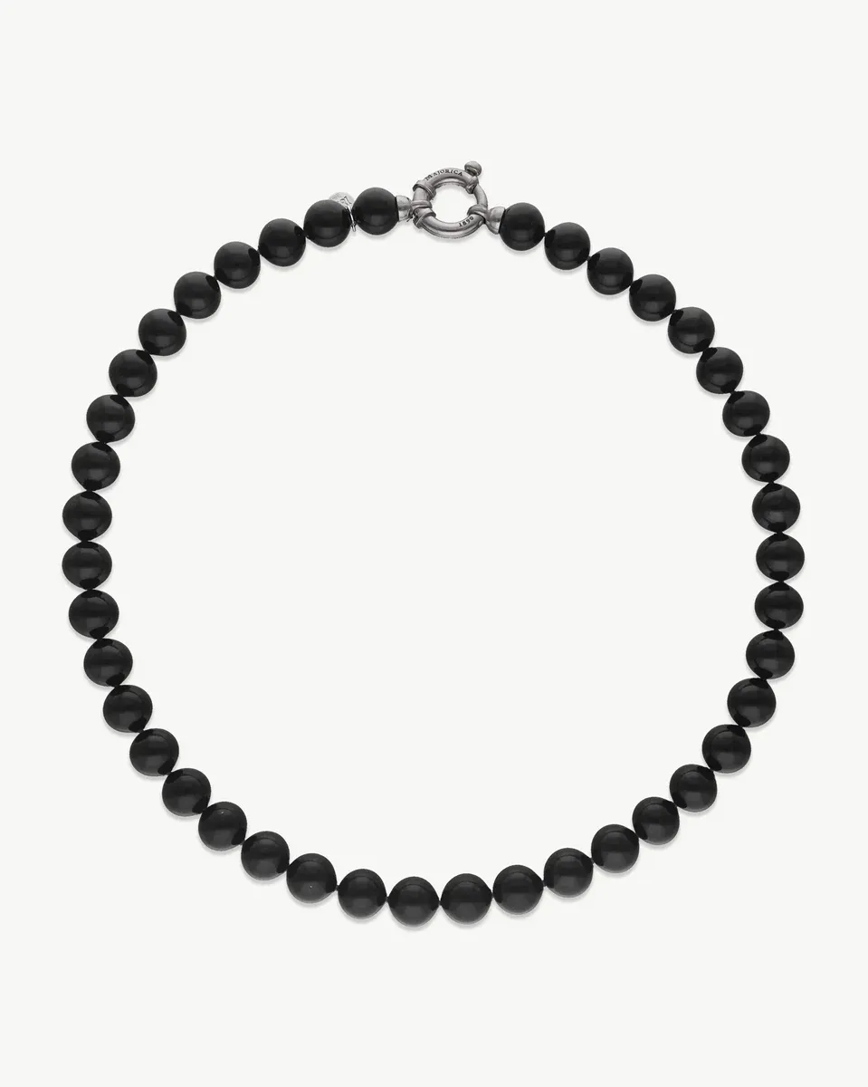 Collar de perlas negras dispuesto en círculo sobre fondo blanco, vista cenital con cierre de plata visible.