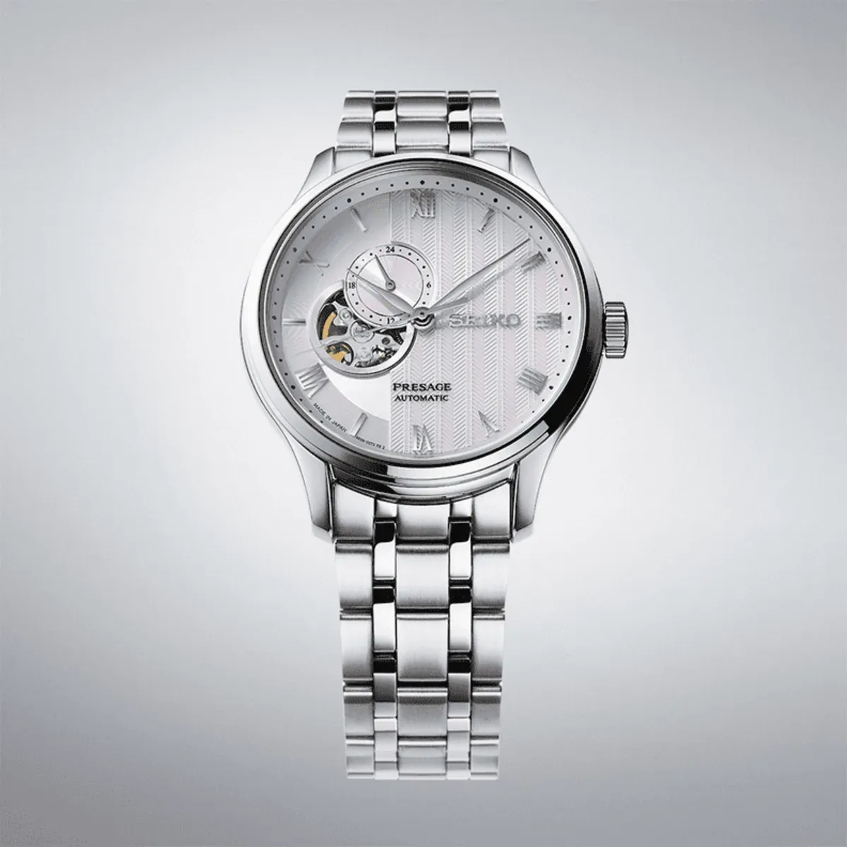 Front view of the watch on a neutral gradient background, showing the textured dial and steel bracelet.