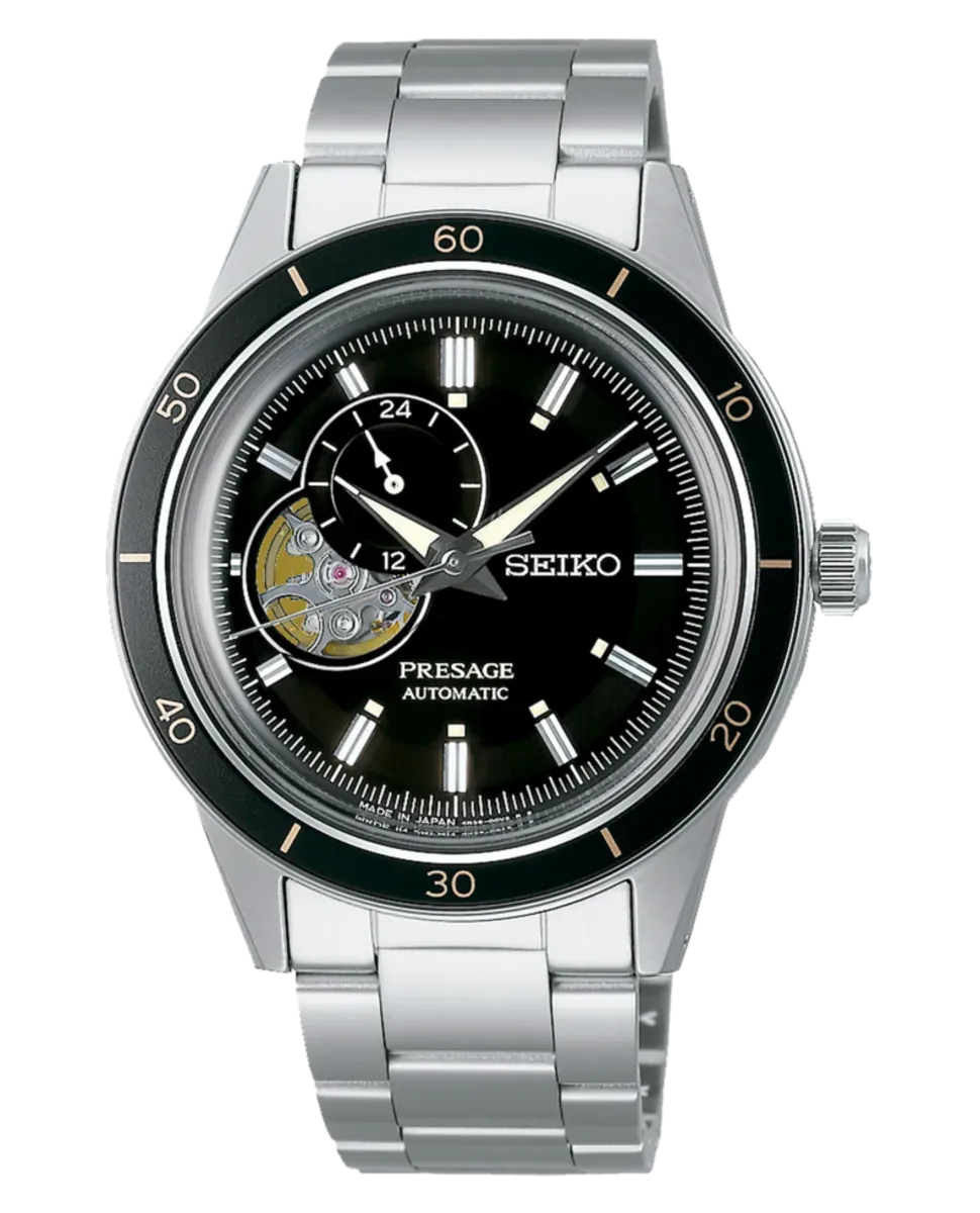 Vista frontal completa del reloj, esfera negra con maquinaria vista y brazalete de acero, fondo blanco.