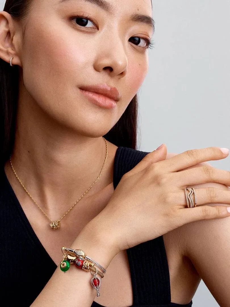 Model mit goldener Halskette, Ring und Armband, Medium-Shot vor neutralem grauem Hintergrund.