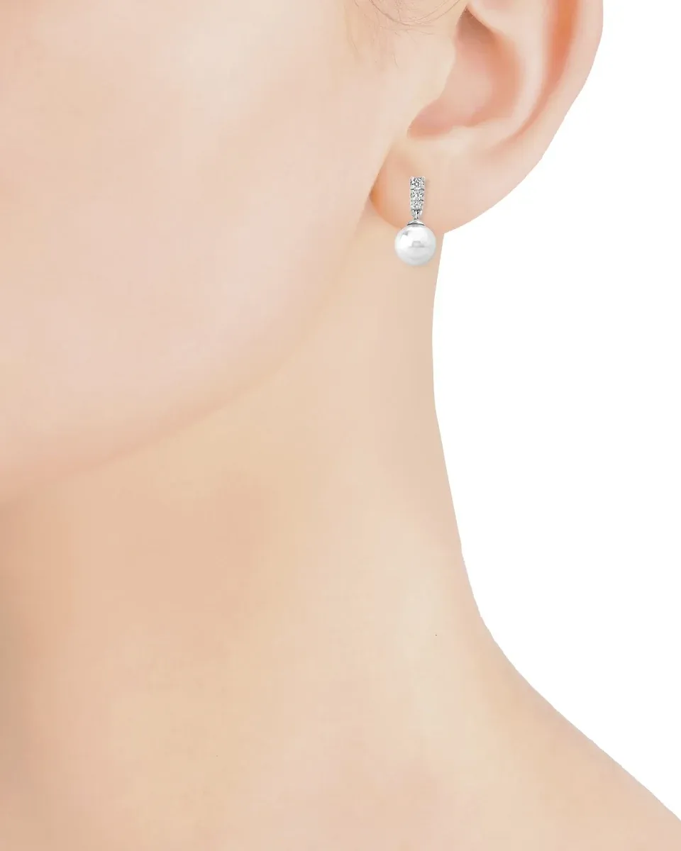 Gros plan de profil d'une boucle d'oreille en perle blanche et zircons portée à l'oreille, fond blanc.