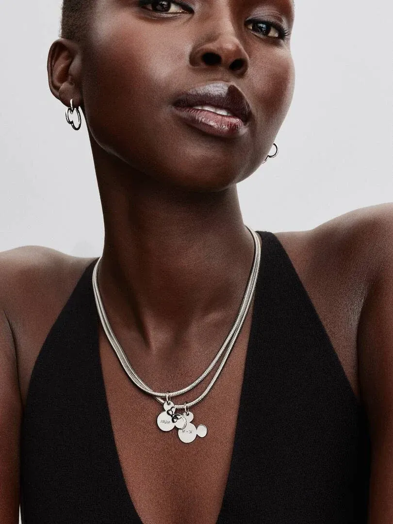 Nahaufnahme der Halskette mit Mickey-Mouse-Anhänger am Model, Frontansicht vor neutralem Hintergrund.